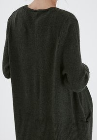 Mörkgrön oversized stickad tröja med en strukturerad yta, ribbad nederkant och fickor, med rundad halsringning och avslappnade ärmar.