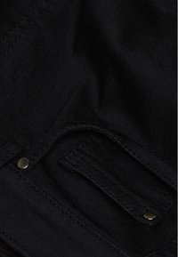 Schwarzer Stoff mit glatter Textur und sichtbaren Nähten. Ein Metallknopf und eine Taschenverzierung sind deutlich sichtbar.