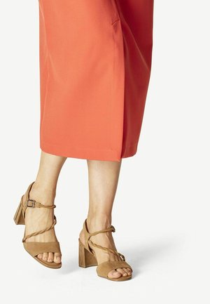 Lysebrune ruskindsandaler med blokhæl, åben tå og snoet remdesign. Bruges med en koralfarvet knælængde nederdel.