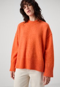 Teksturet, oransje strikkegenser med ribbestrikket nederkant og mansjetter, med en bred, avslappet passform og rund halsutskjæring.