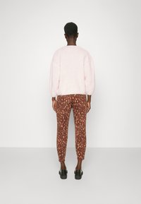 Pink, fluffy sweater with dropped sleeves, paired with brown leopard-print pants. Footwear is black, chunky-sole shoes.