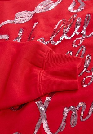 Röd sweatshirt med en strukturerad tyg och glänsande silverpaljetter som bildar vågiga mönster. Ribbad mudd med snug passform.