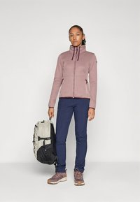 Purple patterned jacket with a high collar, paired with navy pants. Brown hiking shoes and a two-toned backpack, design emphasizes functionality.