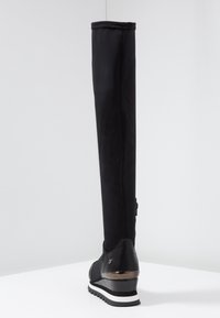 Botte noire montante en tissu lisse, avec un détail de fermeture éclair et une semelle blanche contrastante avec un subtil accent métallique au talon.