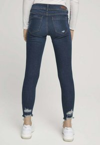 Slim jeans i mörkblå denim med en sliten söm. Har bakfickor och midjehöjd. Matchas med vita sneakers.