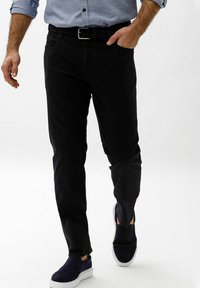 Pantaloni neri in cotone a vestibilità slim con passanti per cintura, dotati di tasche laterali e una texture liscia. Indossati con scarpe slip-on blu navy.