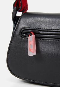 Borsa a spalla nera in ecopelle con chiusura a zip, dotata di un tirazip in plastica rossa e trasparente. Superficie testurizzata con cuciture a vista.