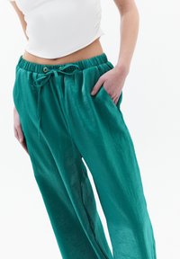 Teal, lichtgewicht, loszittende broek met een elastische tailleband en trekkoord. Heeft een zak aan de rechterkant, gladde textuur.