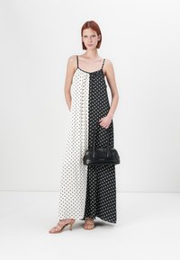 Mustvalge täpiline maksikleid, millel on spagetti rihmad, koos musta käekoti ja beežide sandaalidega. Sile kangastekstuuri, A-lõikega siluett.