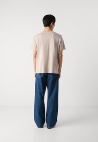 T-shirt beige à manches courtes et jeans en denim bleu oversize à coupe droite. Les jeans présentent des poches arrière visibles et des détails de couture.