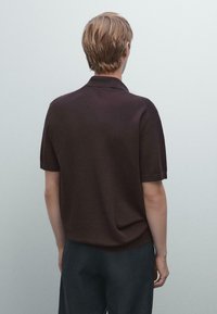 Brun polo skjorte med korte ærmer, der har en standard krave og en glat tekstur, parret med mørkegrå bukser.