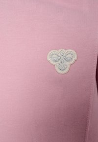 Lichtroze gebreid top met een decoratief wit geborduurd embleem met ingewikkelde patronen. Zachte textuur met een getailleerde pasvorm.