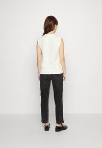 Top de punto blanco sin mangas con un bajo acanalado, combinado con jeans negros de pierna recta. Mocasines negros con detalles decorativos completan el look.