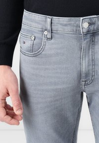 Graue Denim-Jeans mit klassischem Design, ausgestattet mit fünf Taschen, kontrastierenden Nähten und einem kleinen Logo auf der Vordertasche.