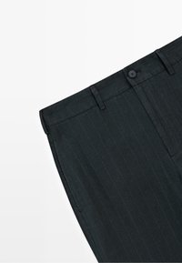 Czarne eleganckie spodnie w cienkie prążki z szlufkami na pasek, zapięciem na guziki z przodu i bocznymi kieszeniami, pokazane na białym tle.