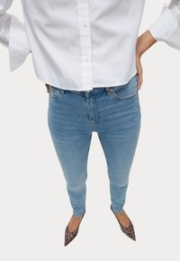 Jeans ajustados de lavado claro con un talle alto, elaborados en denim con un ligero estiramiento; combinados con una camisa blanca de botones y zapatos de punta.
