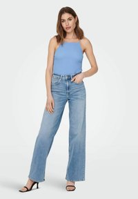 Haut sans manches bleu clair avec un motif texturé, associé à un jean taille haute à jambes larges et délavé, et des talons noirs à lanières.