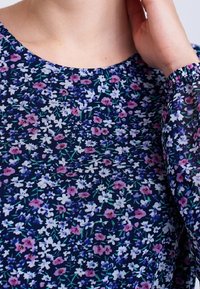 Navy paita, jossa on kukkakuosi vaaleanpunaisilla, valkoisilla ja vihreillä yksityiskohdilla. Materiaali on kevyt pehmeällä pinnalla ja pyöreällä kaula-aukolla.