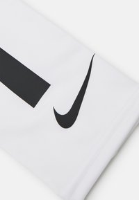 Hvid atletisk ærme med et stort sort Nike-logo og sort vandret stribe. Glat, fleksibelt stof med syning detaljer.