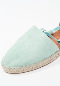 Espadrille de ante verde menta con punta afilada, suela de cuerda de yute y detalles de correa azul claro. Textura suave con un acabado natural.