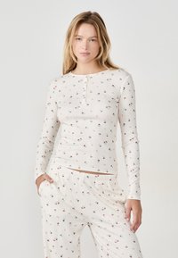 Maglia da pigiama a maniche lunghe in crema con stampa floreale, dotata di scollatura tonda e patta con tre bottoni. Abbinata a pantaloni coordinati.