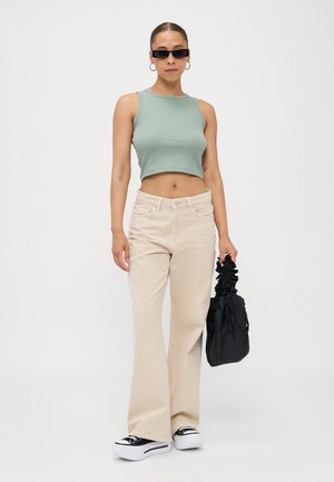 Grünes, kurzes Tanktop, beigefarbene, weite Hose, schwarze Sneakers mit weißen Sohlen und eine schwarze, geraffte Handtasche. Einfaches Design, glatte Textur.