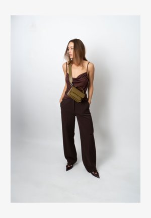 Hnědý top s rolákem, hnědé kalhoty s širokými nohavicemi a boty s špičatou špičkou. Olivově zelená kabelka přes rameno s texturovaným povrchem a nastavitelným popruhem.