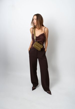 Bruine coltrui, wijde bruine broek en schoenen met een puntige neus. Olijfgroene crossbodytas met een gestructureerde afwerking en verstelbare band.