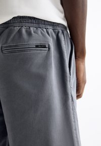 Szare szorty wykonane z miękkiego materiału, z elastycznym pasem, bocznymi kieszeniami i tylną kieszenią na zamek błyskawiczny z detalem logo Pull&Bear.