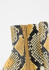 Botte avec un motif serpent noir et jaune, dotée d'une grande fermeture éclair latérale beige. Texture lisse et forme structurée.