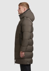 Abrigo acolchado marrón con capucha, que cuenta con un bolsillo lateral con cremallera, textura acolchada y silueta recta. Adecuado para el clima frío.