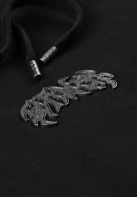 Tessuto nero con una superficie strutturata, caratterizzato da un logo fiamma metallizzato argentato e cordini neri con punte argentate.