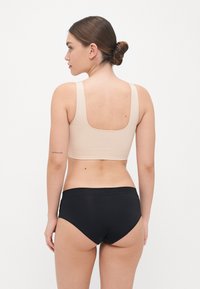 Béžový bezšvíkový crop top so širokými ramienkami a štvorcovým chrbtom, v kombinácii s čiernymi vysokými šortkami. Hladká textúra, minimálny dizajn.