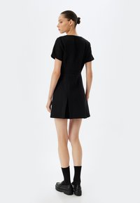 Zwart kortmouwig jurk van gestructureerde stof, met een getailleerde bodice en een uitlopende rok. Bevat een split aan de achterkant voor beweging en een minimalistisch ontwerp.