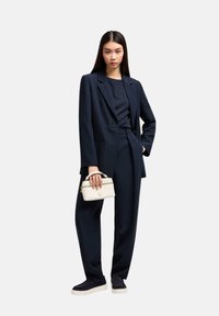 Blazer blazer blu su misura e pantaloni larghi abbinati a una maglietta aderente. Borsa bianca con manico superiore. Sneakers classiche. Design minimalista.