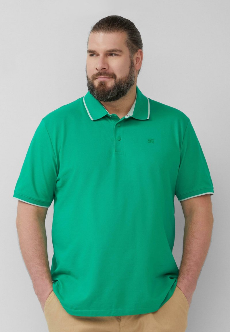 Polo vert avec une finition texturée. Il possède un col avec un bord blanc et trois boutons au niveau du cou. Manches courtes, sans motifs.
