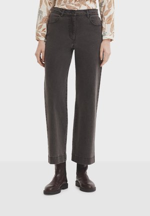 Hoch geschnittene, gerade schwarze Jeans mit leicht ausgewaschenem Stoff und umgeschlagenen Säumen, kombiniert mit dunklen Knöchelstiefeln.