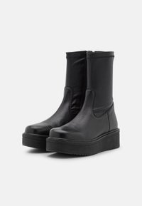 Bottines noires avec une tige en cuir lisse, des panneaux latéraux élastiques et une semelle plateforme épaisse. Le design inclut une fermeture éclair à l'arrière.