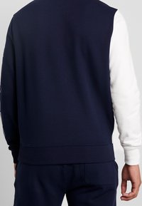 Felpa blu navy con maniche bianche, polsini a costine e scollatura bassa. Caratterizzata da una texture liscia e una vita aderente.