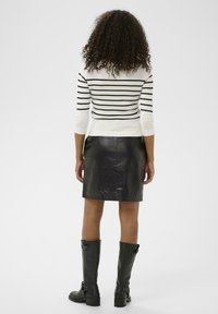 Pull rayé noir et blanc, ajusté, manches trois quarts ; jupe en cuir noir, texture lisse ; bottes hautes noires avec détail de boucle.