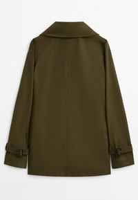 Manteau vert olive avec un large col, des manches ceinturées et une coupe droite. Tissu lisse avec un design épuré et minimaliste. Vue de dos.