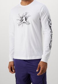 Valkoinen pitkähiha paita, jossa musta graafinen siluetti- ja roiskekuvio edessä ja oikeassa hihaosassa.