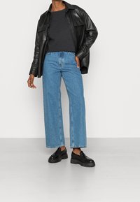 Black leather button-up shirt, dark gray knit top, light wash wide-leg jeans, and black chunky loafers. Smooth textures and contrasting colors.