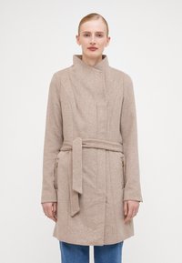 Beige villa segu segu kilekonnaga, mis on varustatud mandariini kaeluse, sidumisrihma ja külgmiste lukudega. Omab struktureeritud õmblusi ja sileda tekstuuri.