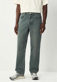 Jean en denim bleu délavé avec une coupe droite, cinq poches et une texture légèrement usée, associés à des baskets grises et blanches.