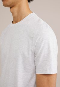 Camiseta gris de cuello redondo hecha de una tela ligera y texturizada. Manga corta y corte relajado, con un sutil patrón jaspeado.