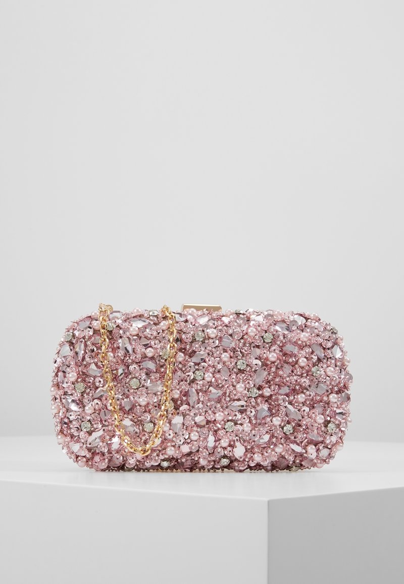 Pochette rectangulaire rose ornée de perles, cristaux et perles de rocaille, avec une chaîne en or, posée sur un piédestal blanc.