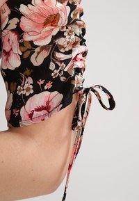 Černá látka s velkým růžovým květinovým vzorem, s bočními řasením a zavazováním jako akcent; strukturovaný a přiléhavý design.