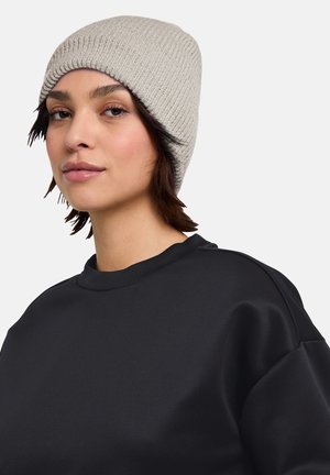 Bonnet en tricot beige avec une texture côtelée, porté avec un sweatshirt noir à col rond. Design simple, coupe ajustée, et tissu doux.