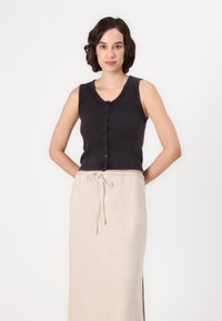 Top nero a costine con chiusura a bottoni, abbinato a una gonna maxi beige con cordoncino caratterizzata da una sottile texture e uno spacco laterale.